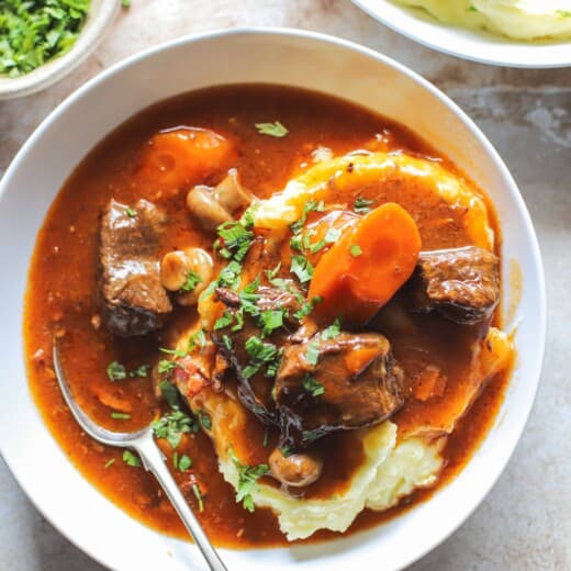 close up of beef bourguignon in a bowl over mashed potatoes