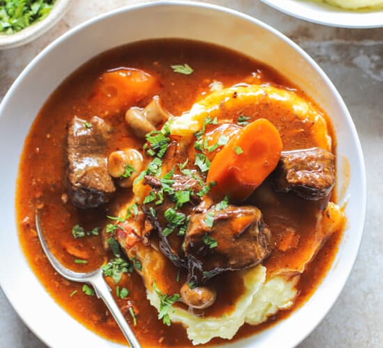 close up of beef bourguignon in a bowl over mashed potatoes