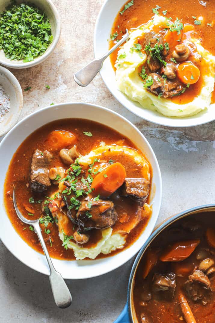 Two servings of slow cooker beef bourguignon beside a crock of the remaining stew