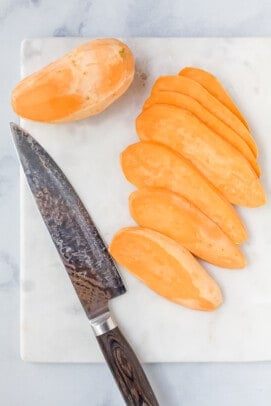 Sliced sweet potatoes next to a knife on a cutting board.