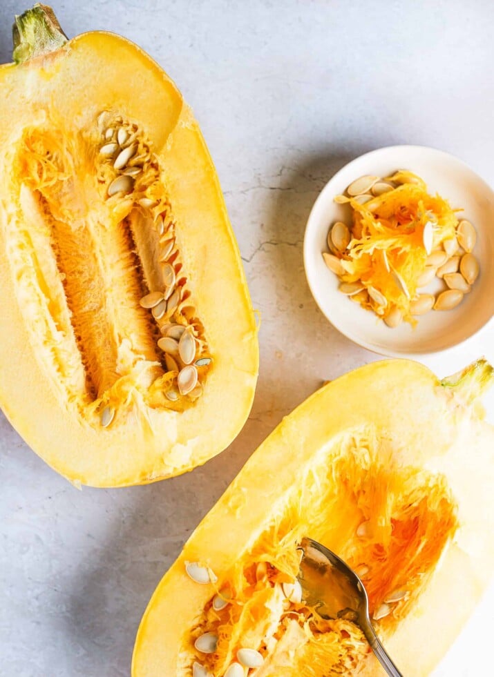 Two halves of a spaghetti squash on a countertop with a spoon scraping out the seeds