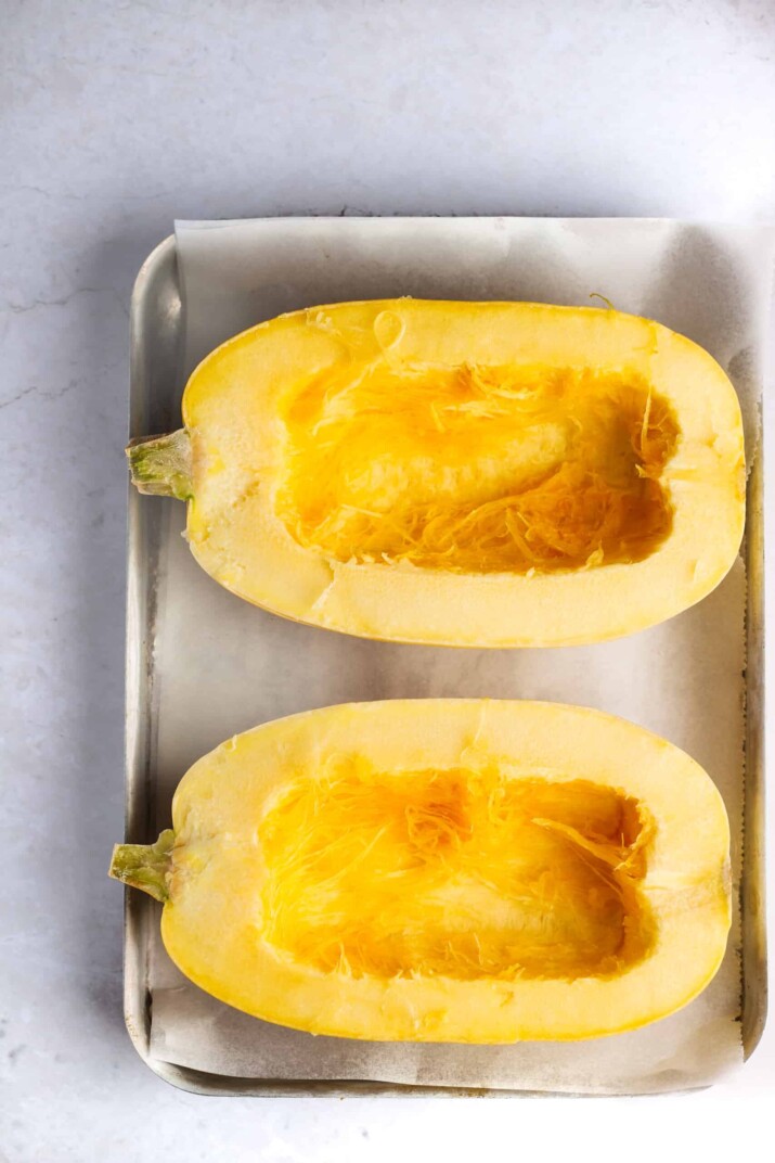 A halved spaghetti squash on a rimmed baking sheet lined with a piece of parchment paper