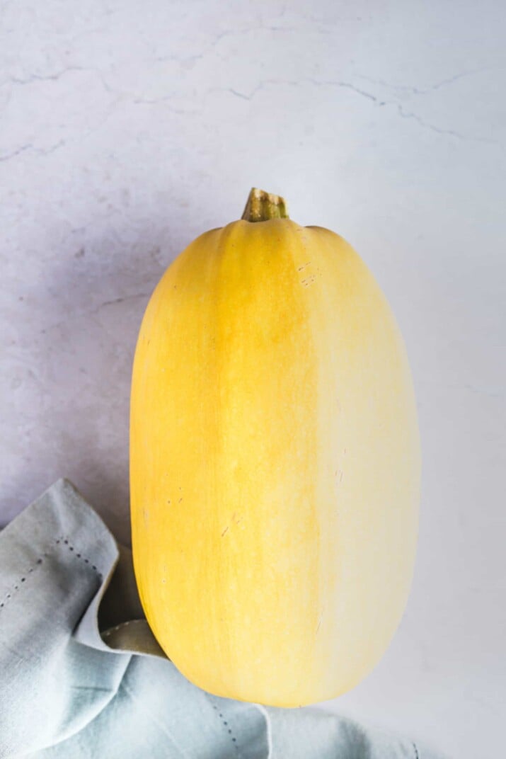 A raw spaghetti squash on a granite countertop beside a baby blue kitchen towel