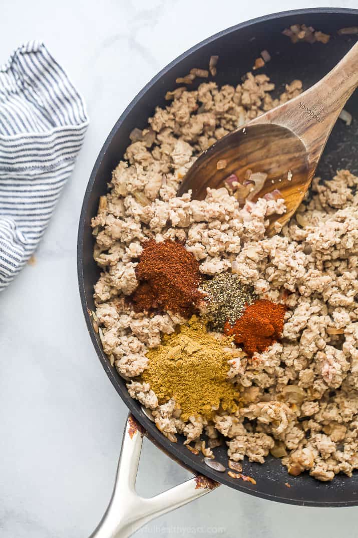 Ground turkey inside of a metal skillet with cumin, chili powder and the rest of the spices
