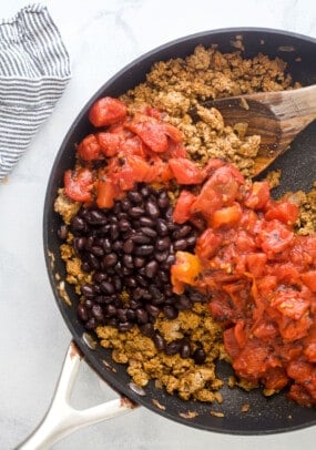 Seasoned ground turkey in a skillet with fire roasted tomatoes and drained black beans on top