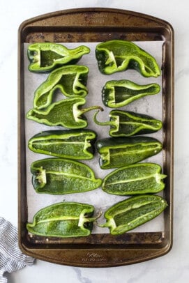 12 poblano pepper halves arranged on a baking sheet lined with parchment paper