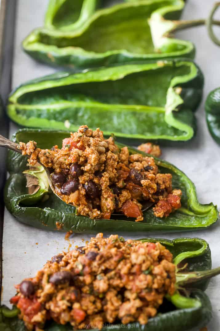Two poblano peppers with the ground turkey filling added beside two empty pepper halves