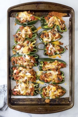 Six halved poblano peppers arranged filling-side up on a baking sheet with melted cheese on top