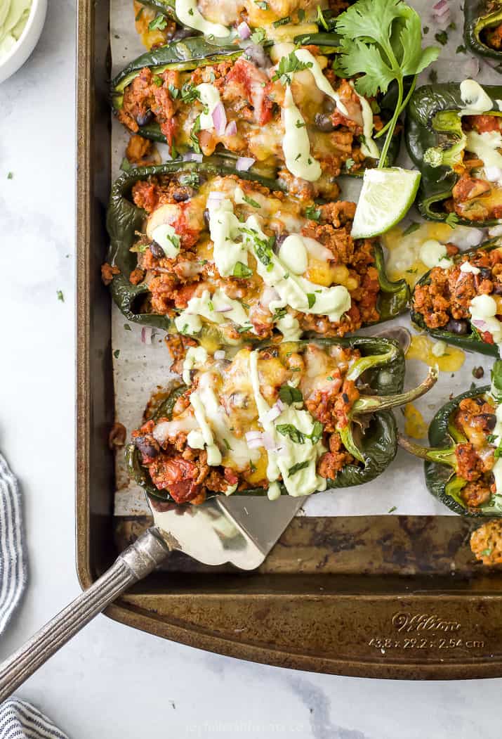 A baking sheet full of turkey stuffed poblano peppers topped with avocado crema and chopped cilantro