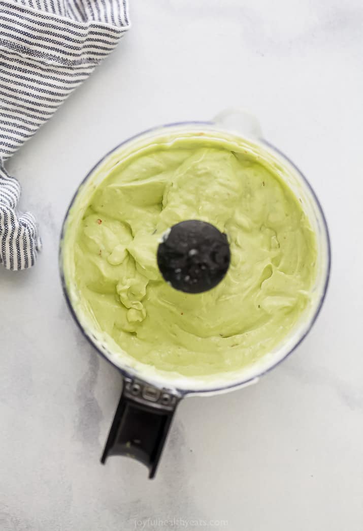 Smoothly combined avocado crema inside of a small food processor on a white countertop