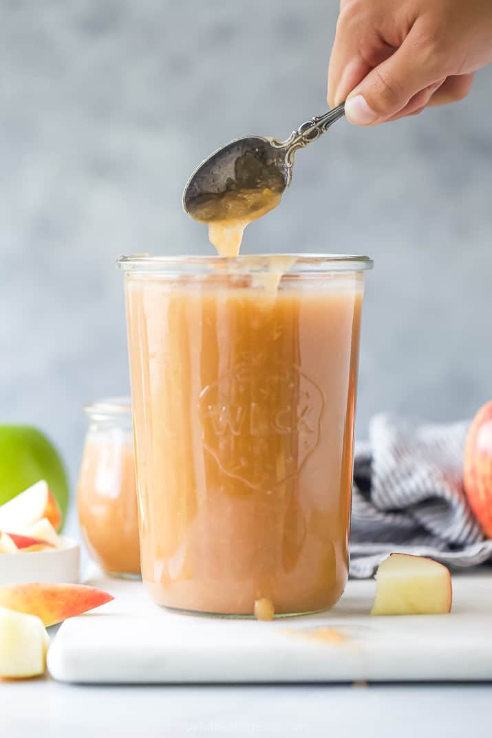 A metal spoon digging into a jar of homemade applesauce with a second jar of applesauce in the background