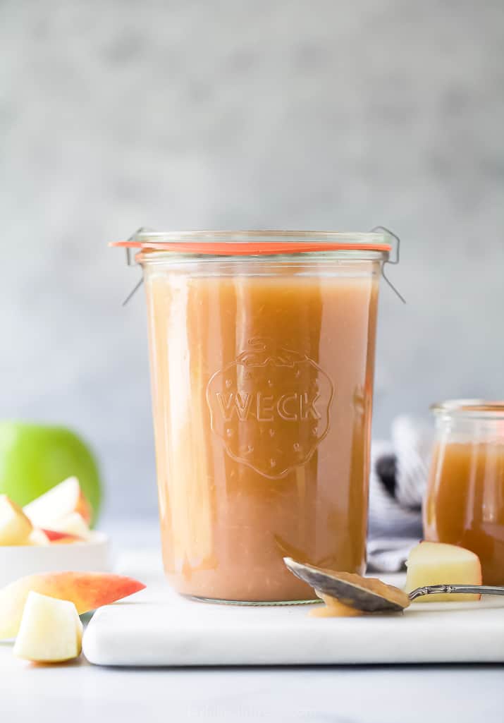 A glass jar on an off-white cutting board containing homemade applesauce