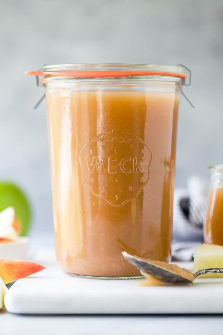 A jar filled with homemade apple sauce with fresh apple slices beside it