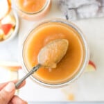 A bite of unsweetened Instant Pot applesauce on a spoon hovering above a full jar