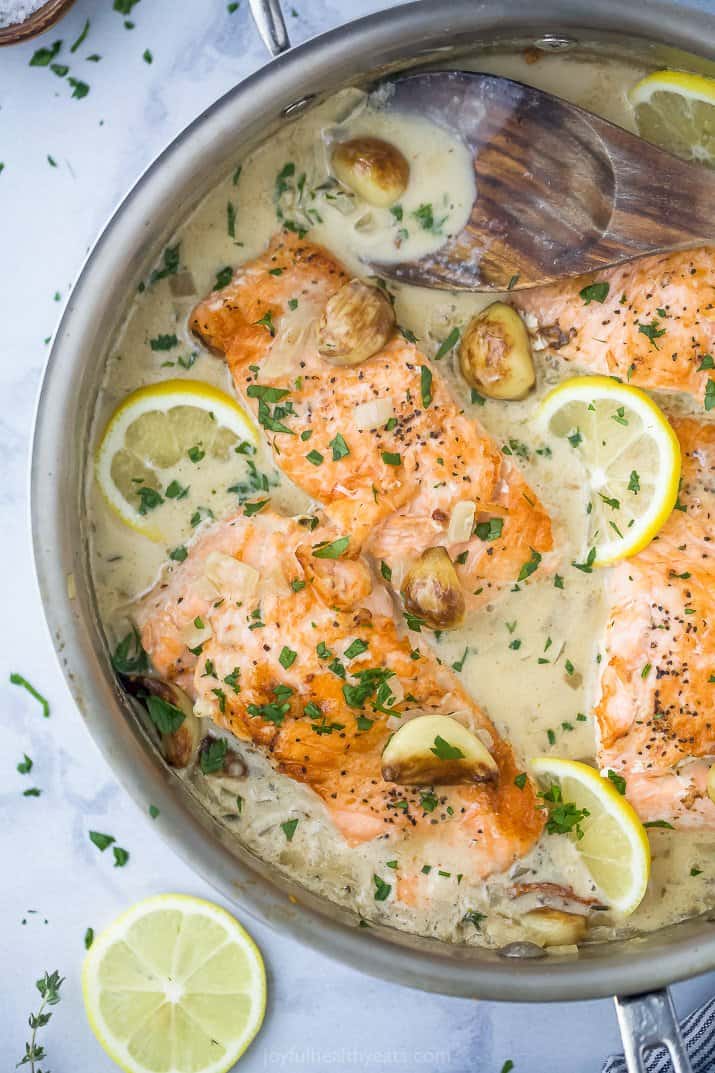 Salmon filets in a garlic cream sauce with lemon wedges.