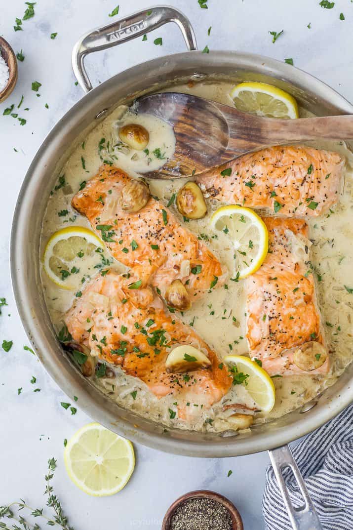 Salmon filets in a pan full of garlic cream sauce.