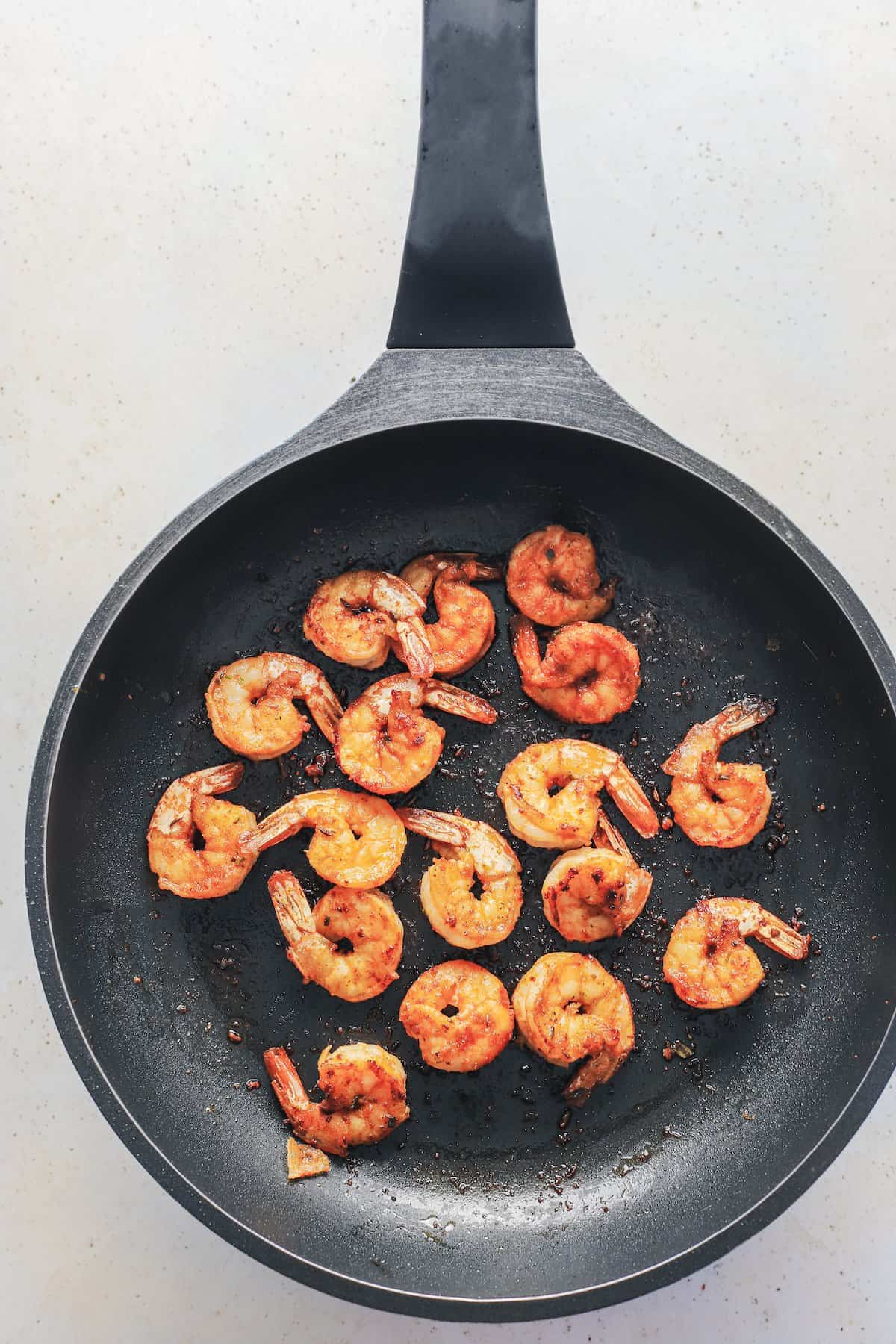Seventeen shrimp being cooked inside of a large black skillet with olive oil inside of it