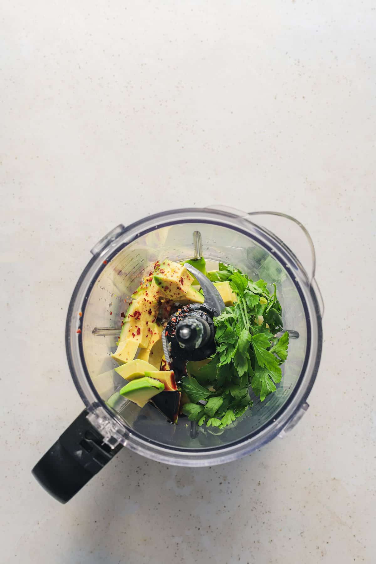 The guacamole ingredients inside of a food processor on the counter