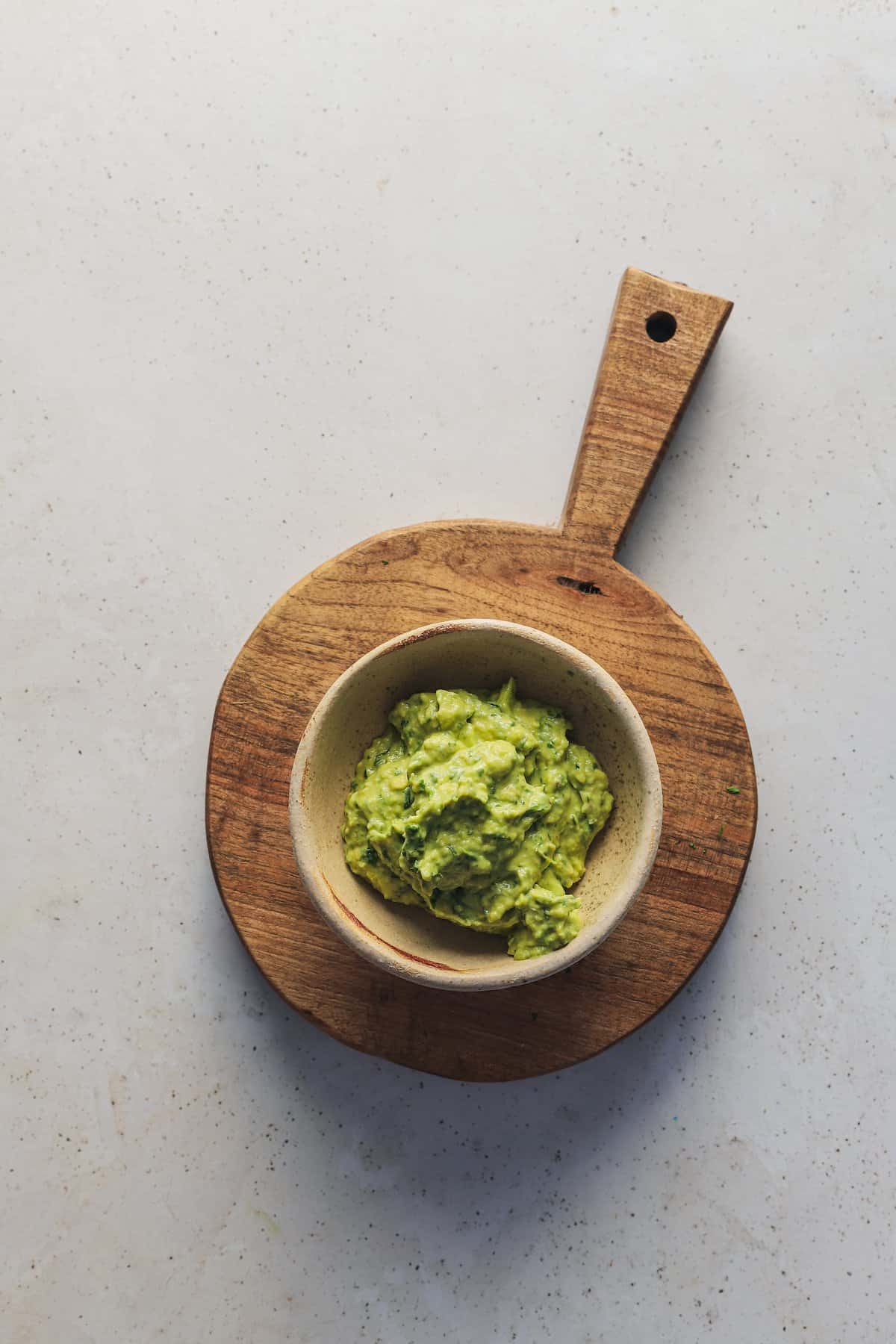 A small bowl of guacamole on top of a round wooden stand with a handle