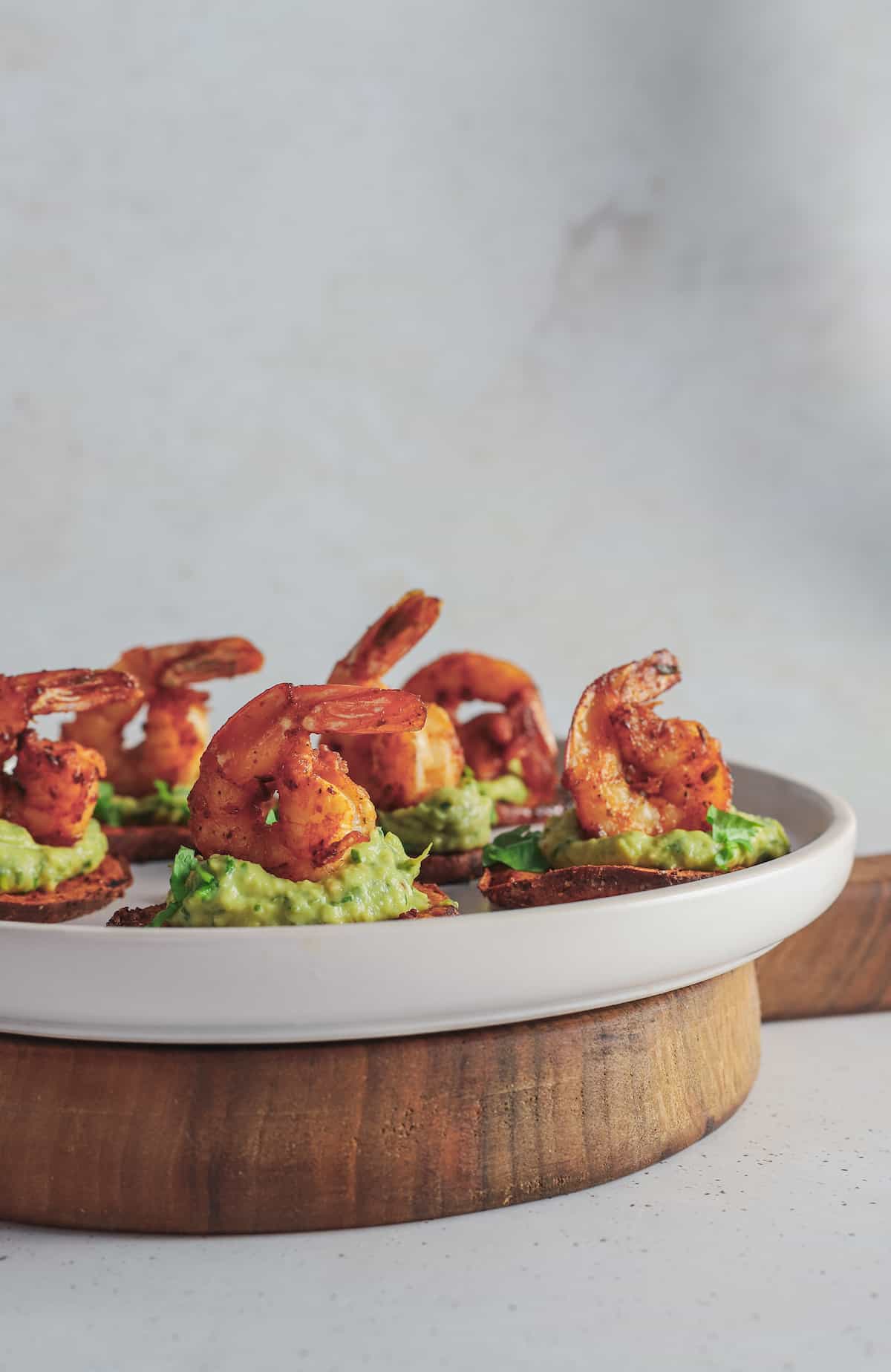 A plate of seafood appetizer bites on a wooden stand with a white wall in the background