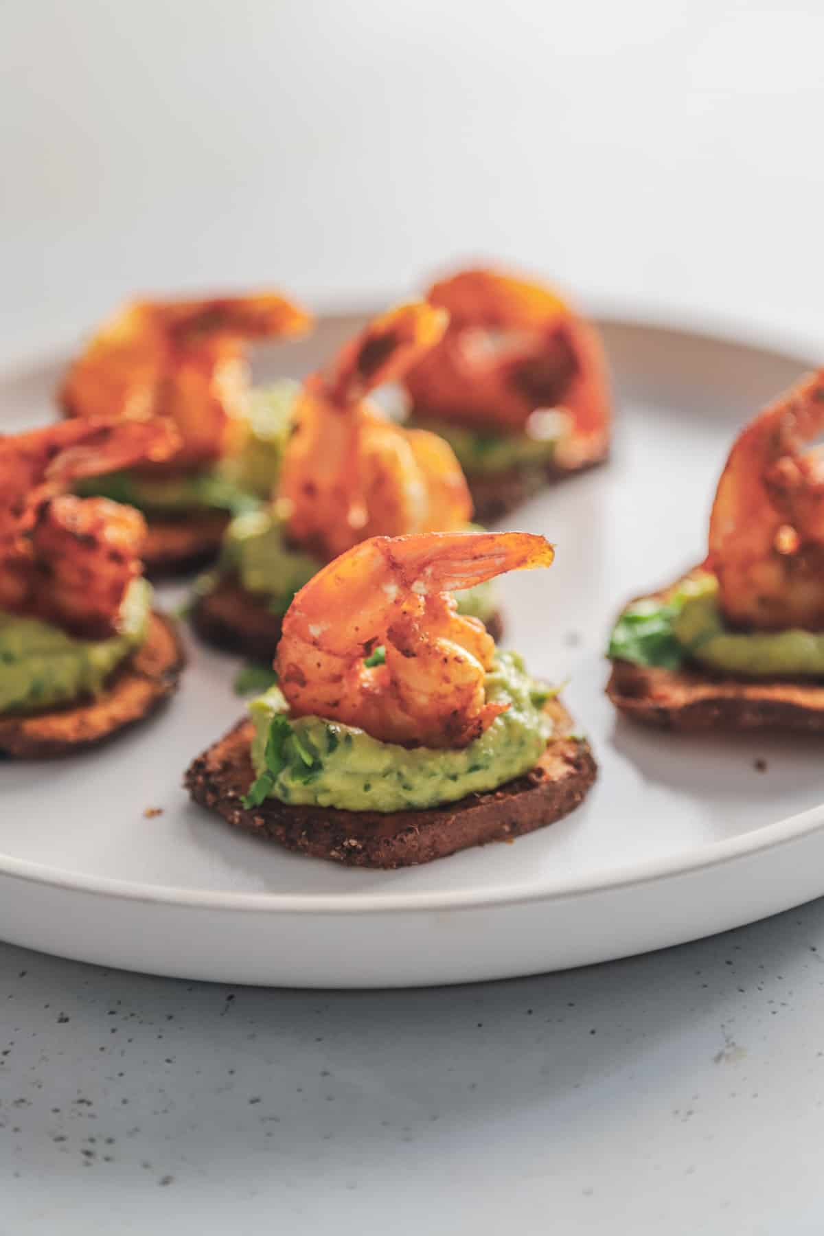 A white plate full of cajun shrimp guacamole bites on a countertop