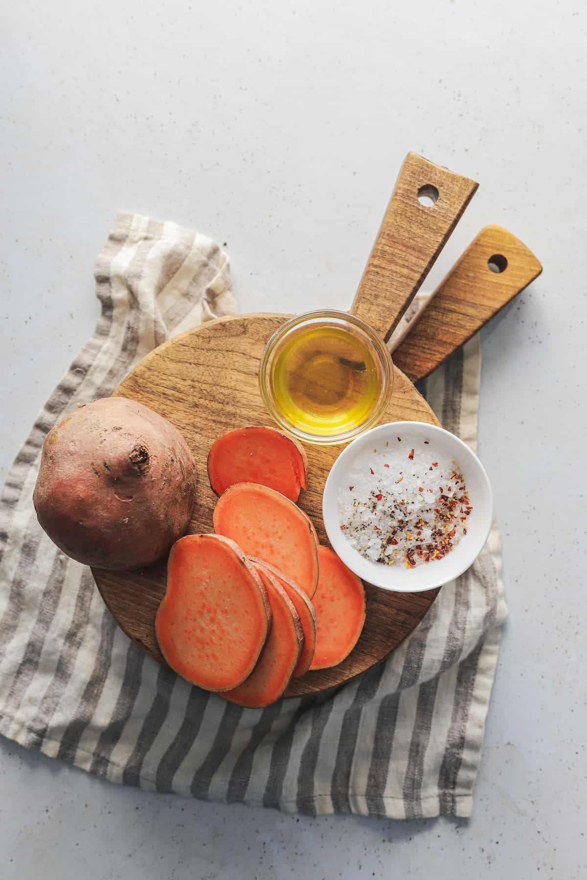 Sliced sweet potato on a wooden stand beside a dish of oil and a dish of salt