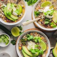 Three bowls on a countertop containing white chicken chili with spoons inside two of them
