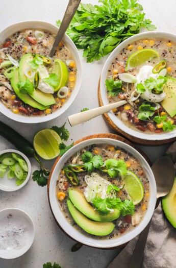 Three bowls on a countertop containing white chicken chili with spoons inside two of them