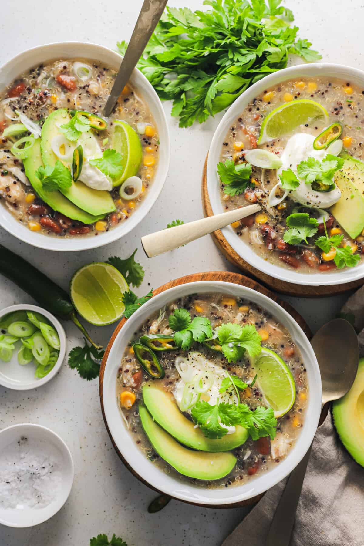 Three bowls on a countertop containing white chicken chili with spoons inside two of them.