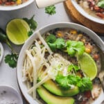 A close-up shot of a bowl of homemade white chicken chili with a lime slice and a dish of salt beside it