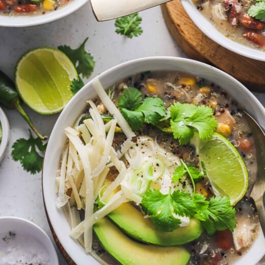 A close-up shot of a bowl of homemade white chicken chili with a lime slice and a dish of salt beside it