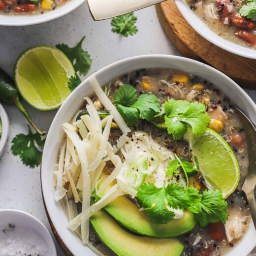 A close-up shot of a bowl of homemade white chicken chili with a lime slice and a dish of salt beside it