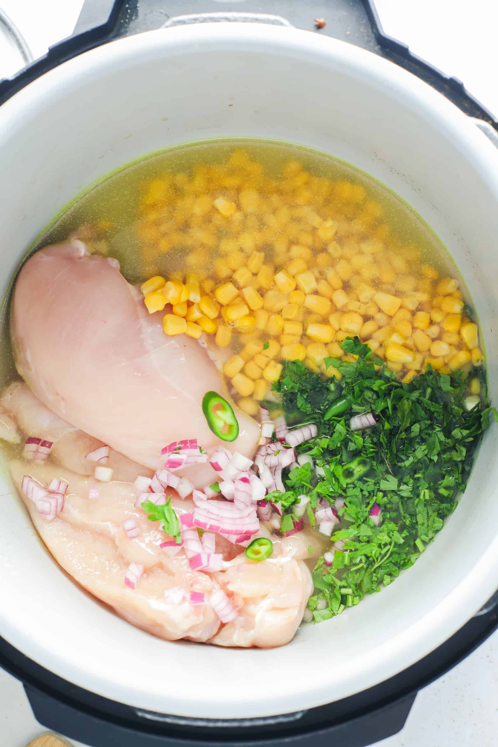 Raw chicken, frozen corn, water, broth, cilantro, onions, chilis, garlic, cumin, and cilantro in the inner pot of a slow cooker.
