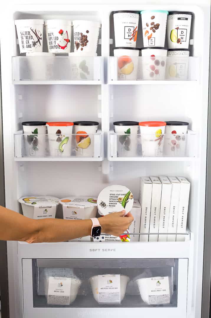 A fridge filled with Daily Harvest food with a hand reaching in to get something.