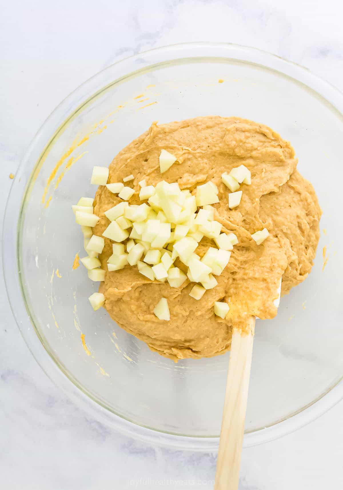 The nearly-completed batter in a glass mixing bowl with diced Granny Smith apples on top