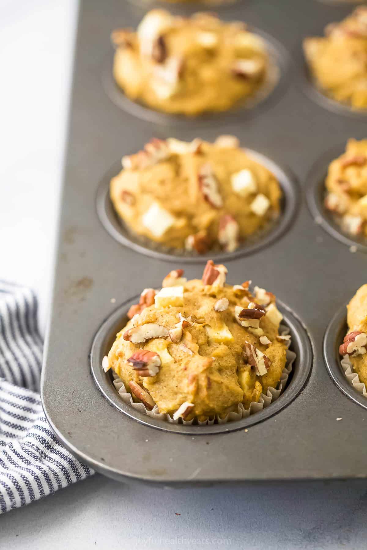 Three homemade muffins inside a muffin tin next to a striped kitchen towel