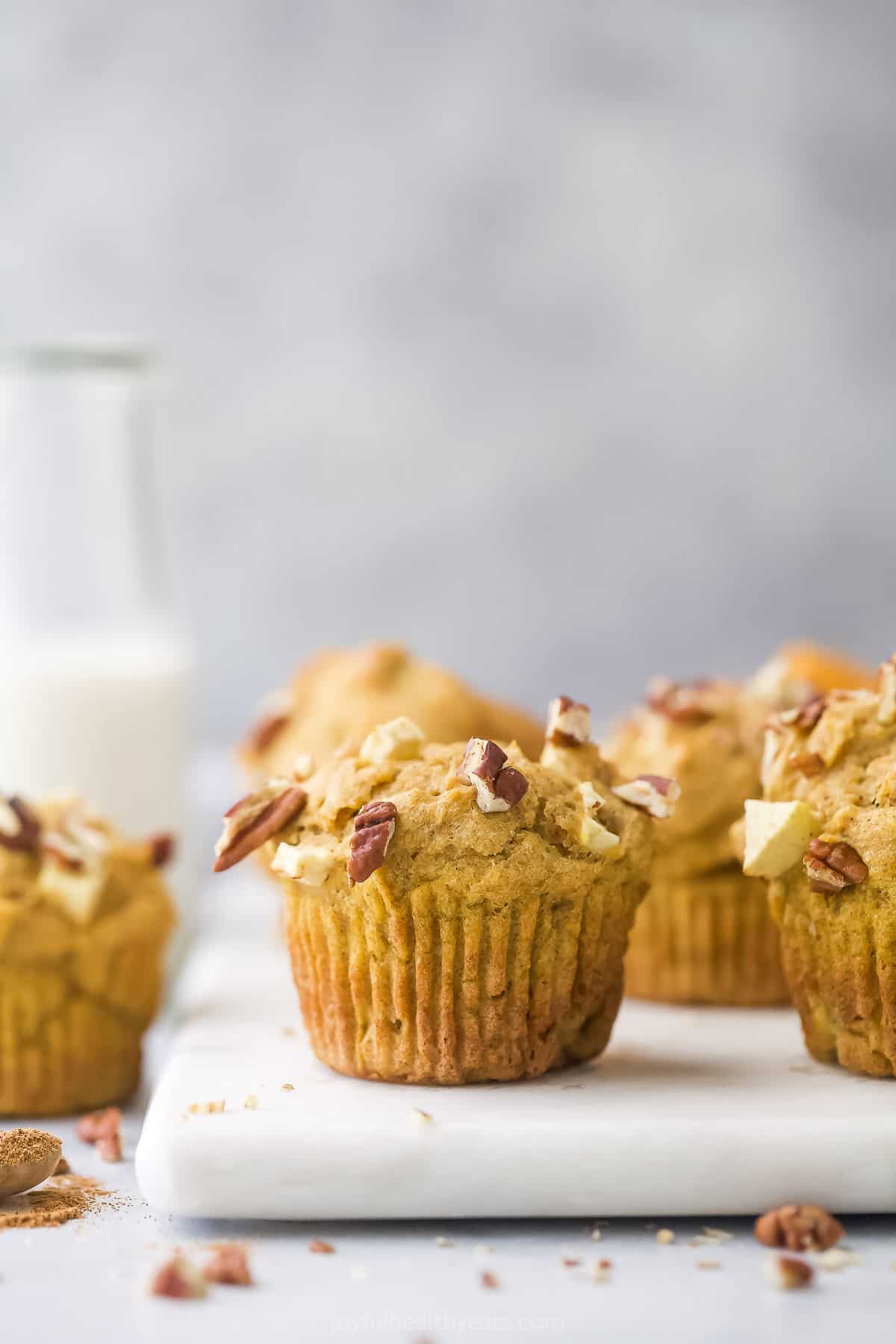 A white cutting board holding freshly baked apple pumpkin muffins with chopped pecans on top