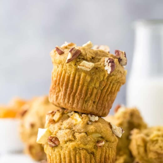 Two apple pecan muffins stacked on top of one another with a glass of milk behind them