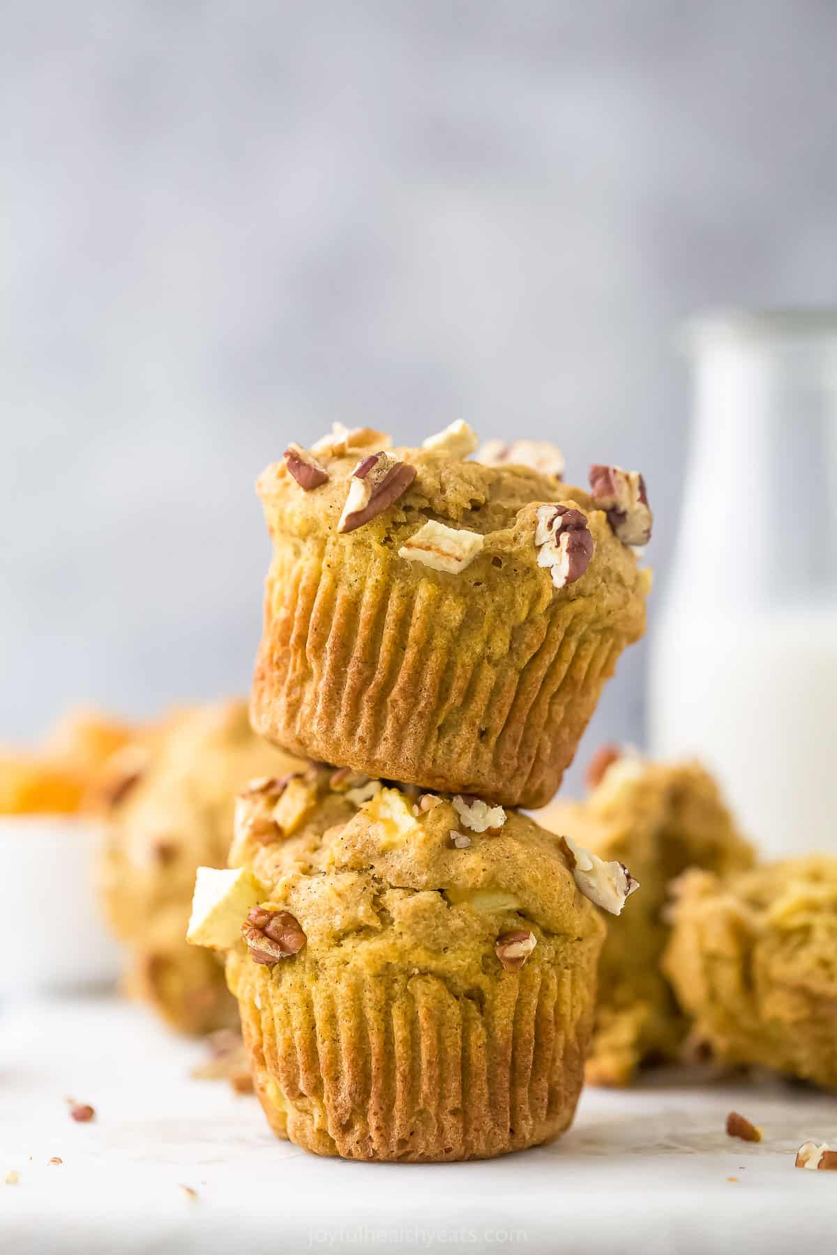 Two apple pecan muffins stacked on top of one another with a glass of milk behind them