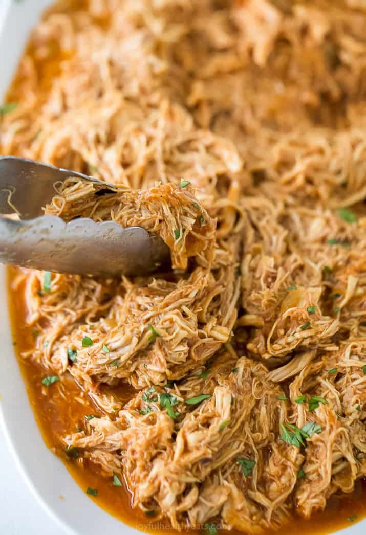 tongs picking up shredded bbq chicken on a plate