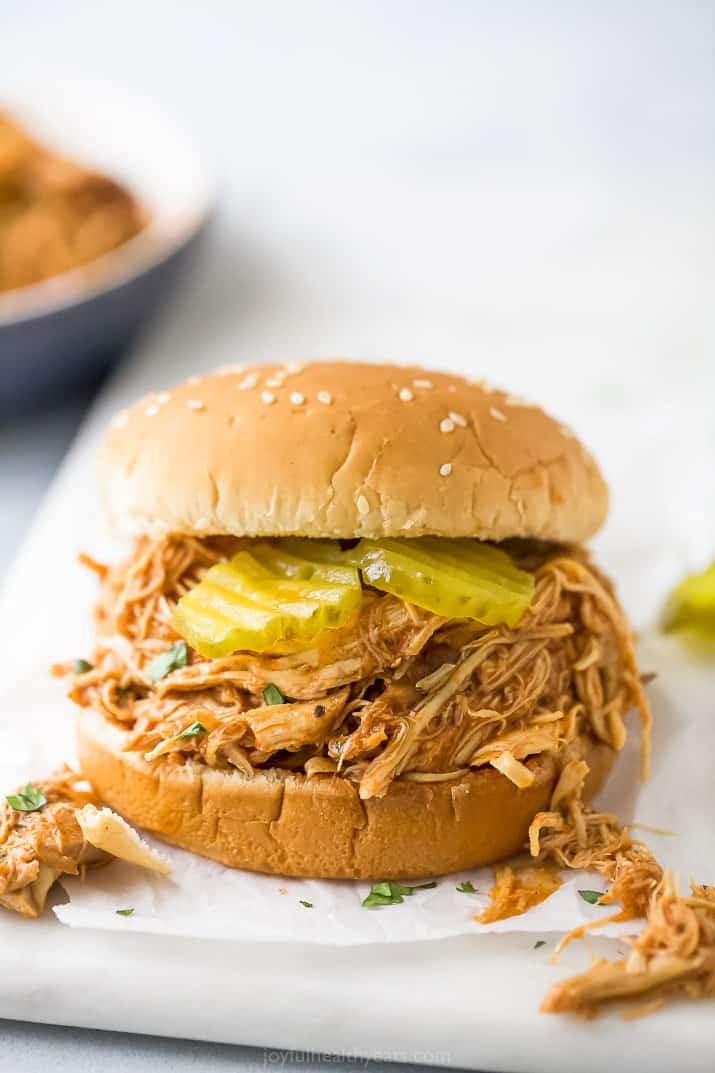 A shredded chicken sandwich on a white cutting board