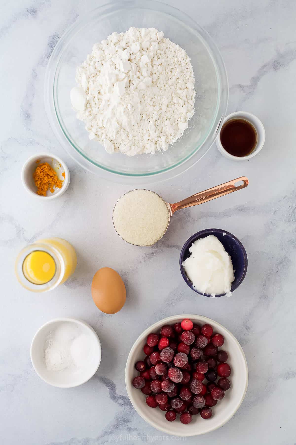 A bowl of gluten-free flour, an egg, coconut oil and the remaining muffin ingredients on a marble countertop
