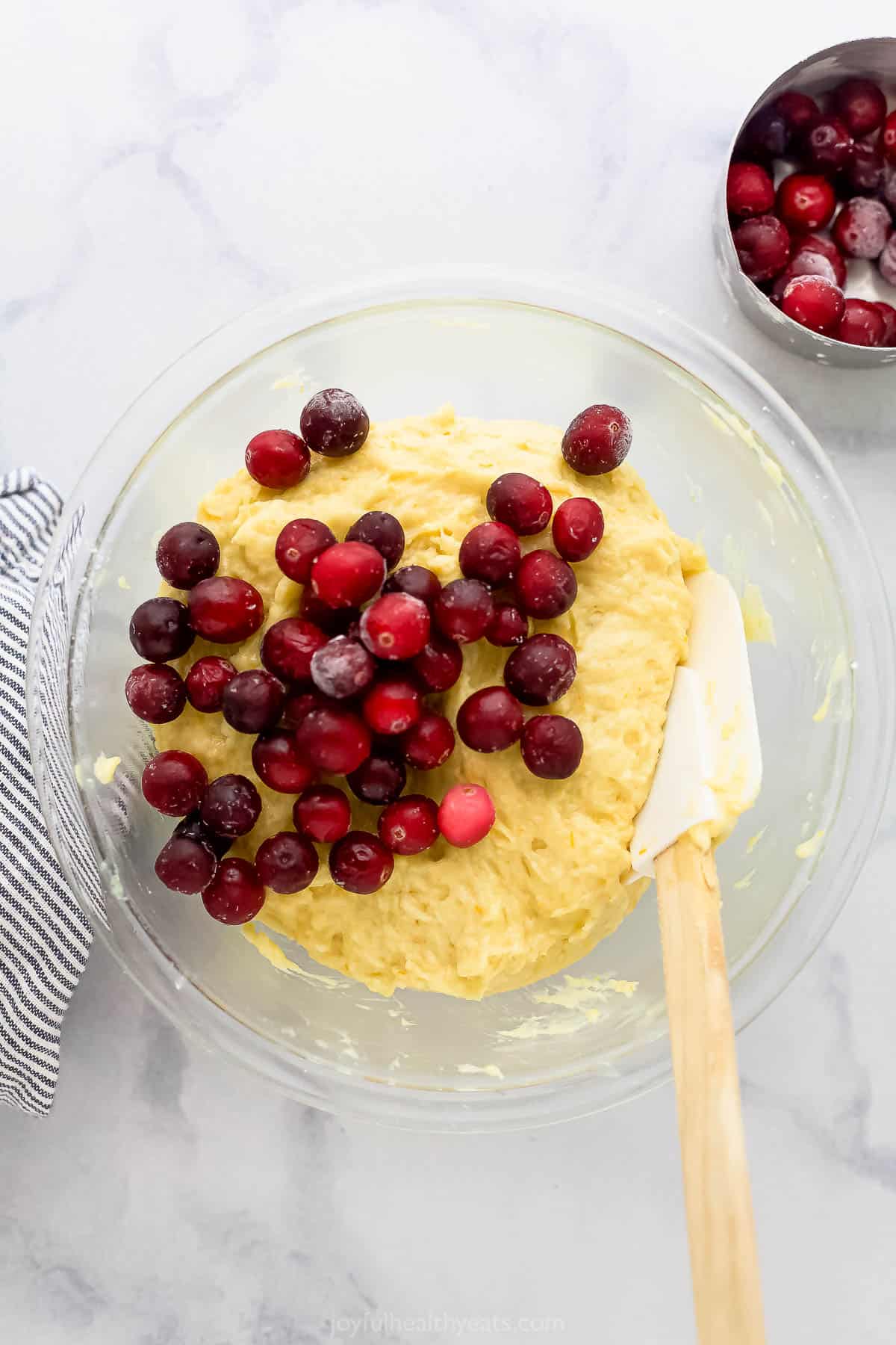 The combined muffin batter in a glass bowl with fresh cranberries on top