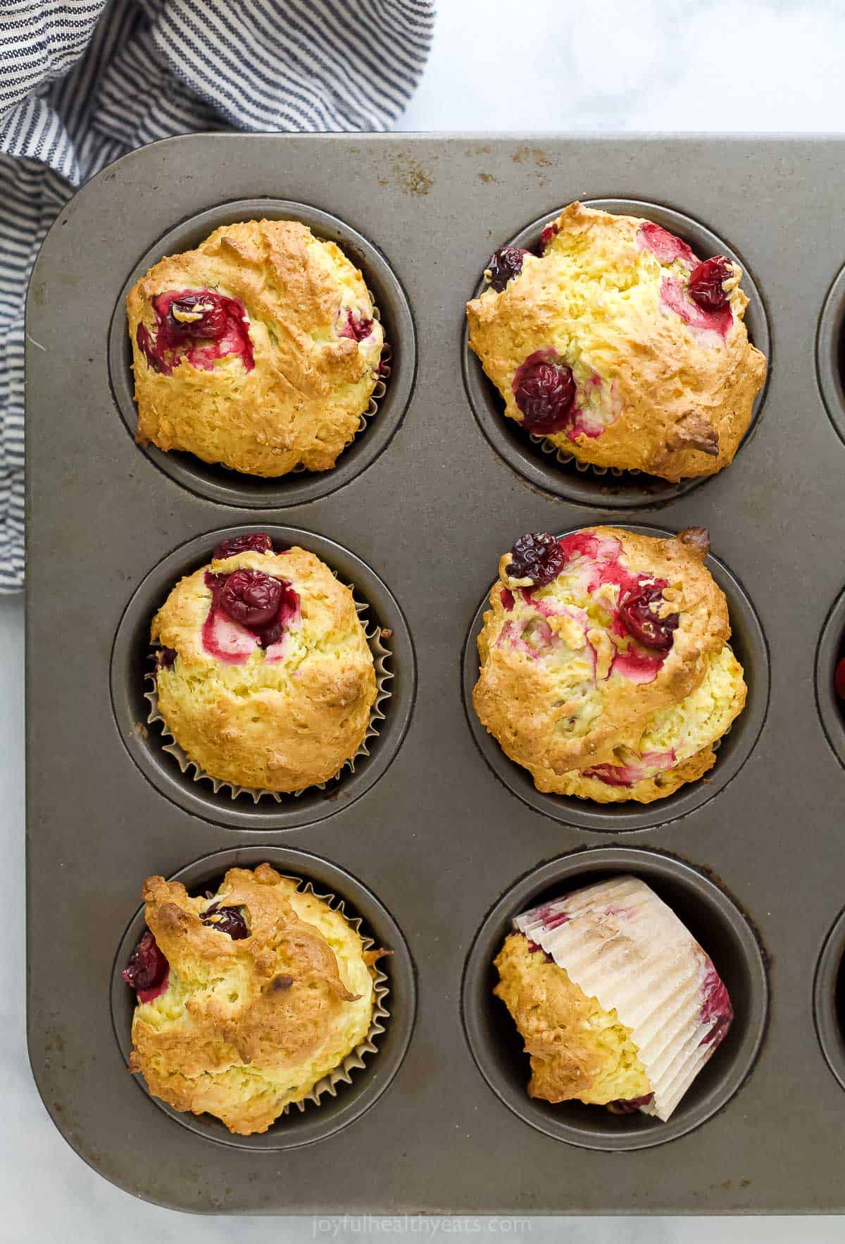 A cupcake tin containing twelve cranberry muffins with six outside of the frame