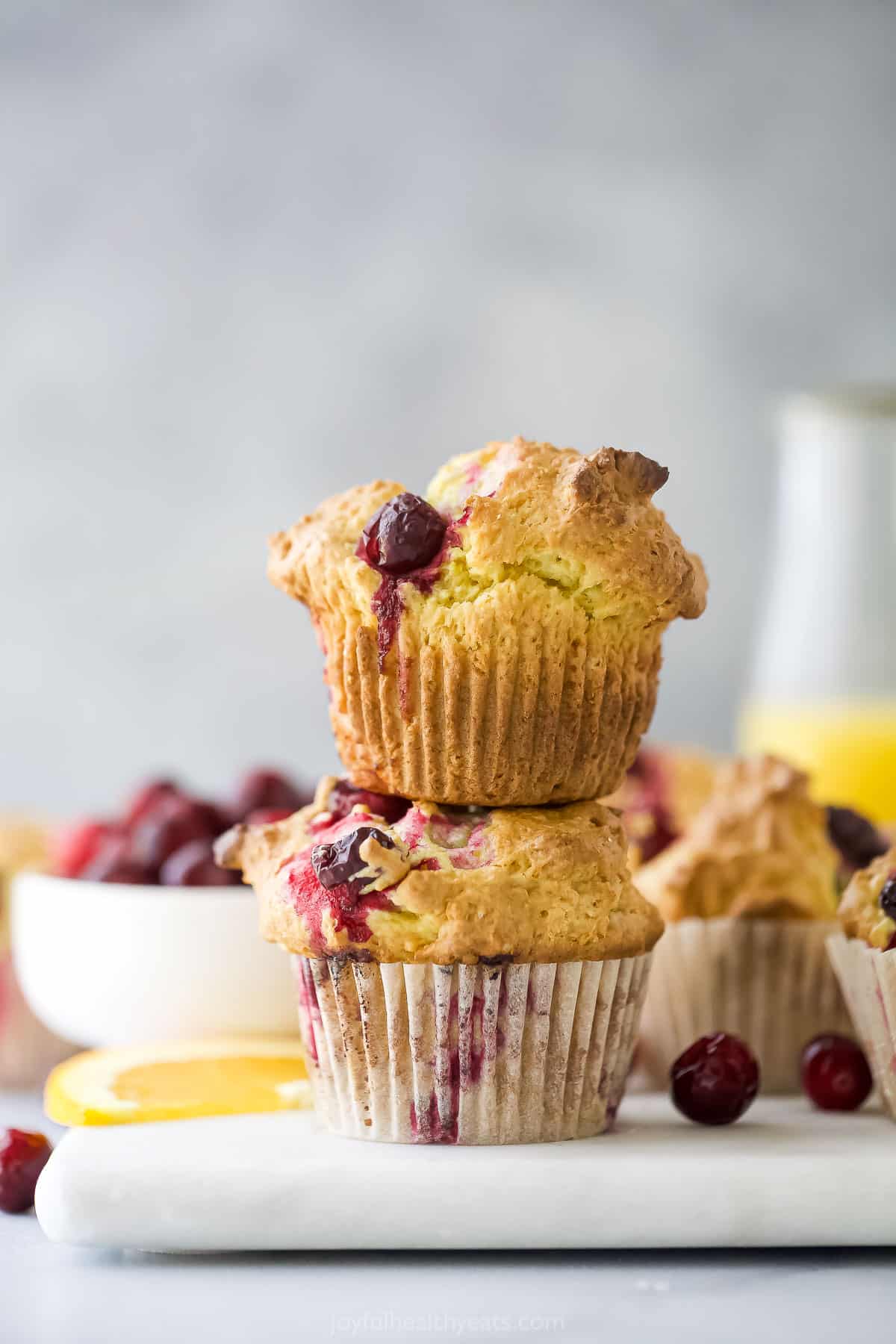 Two cranberry orange muffins stacked on top of a white cutting board