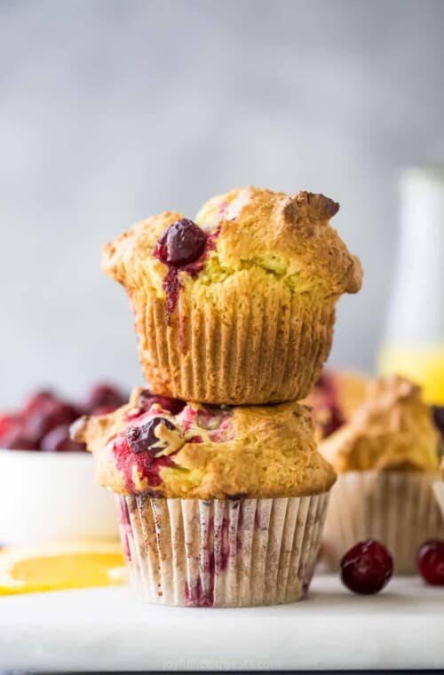 A close-up shot of a stack of two cranberry orange muffins on top of a cutting board