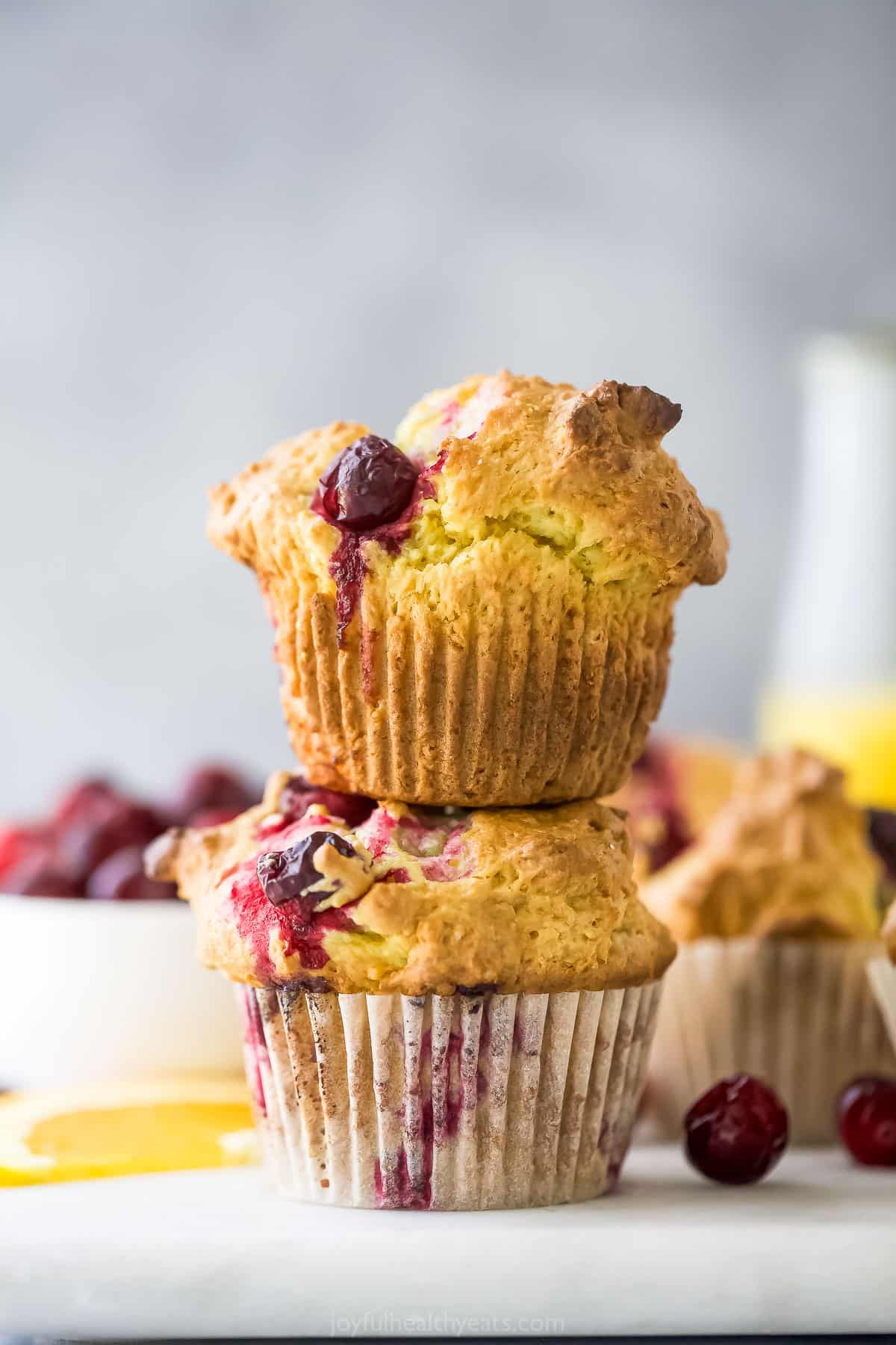 A close-up shot of a stack of two cranberry orange muffins on top of a cutting board