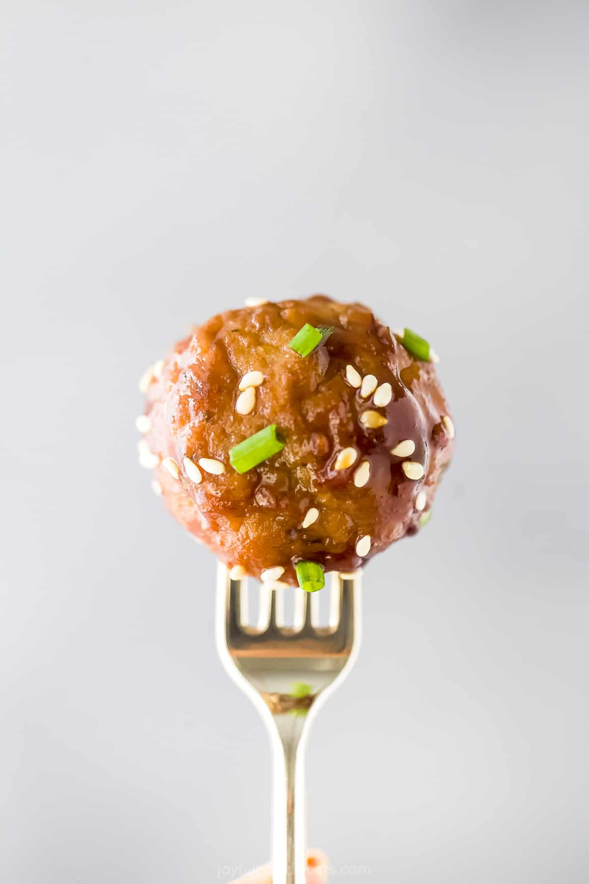 A single Asian meatball being held by a fork in front of a white wall