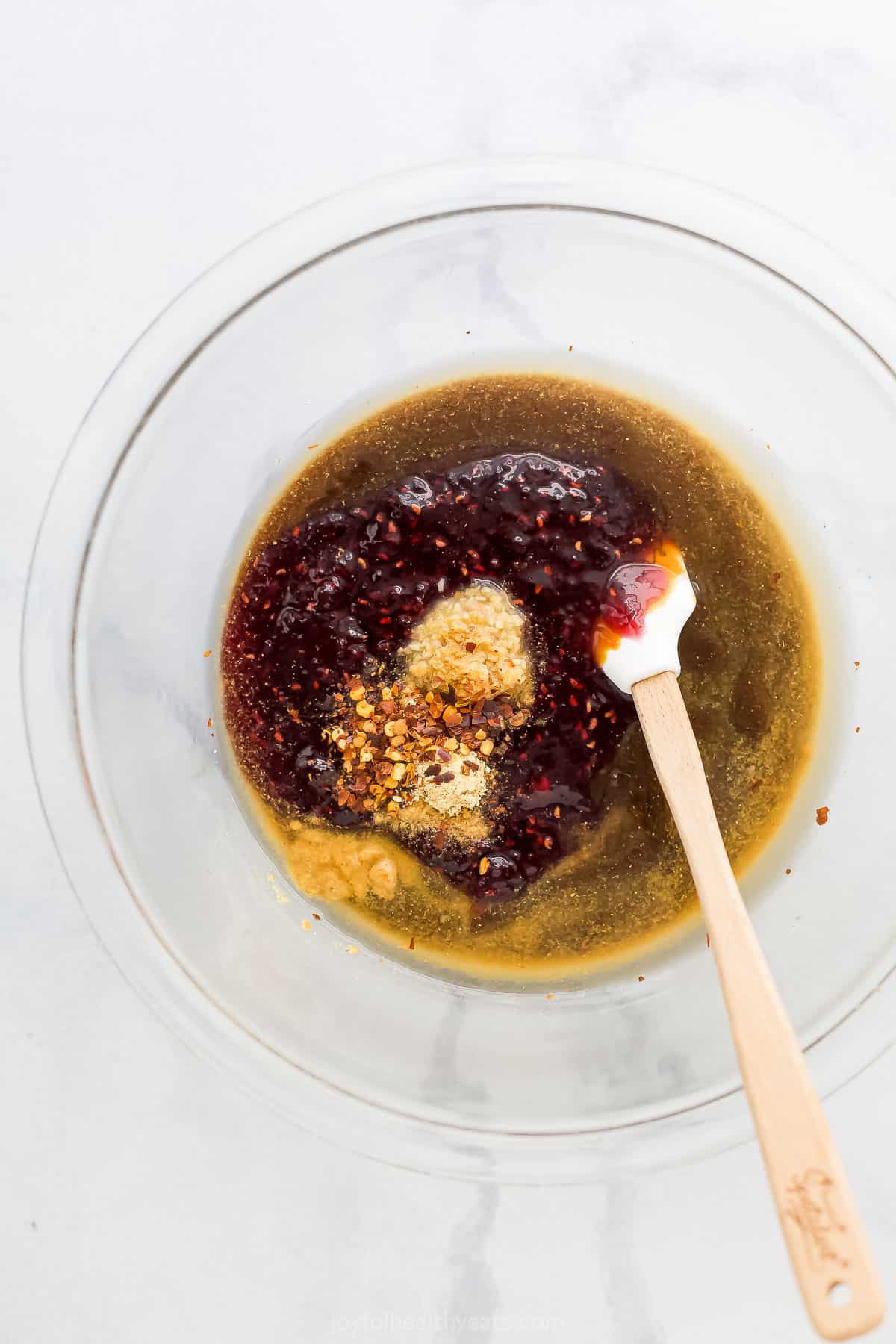 The sauce ingredients in a glass mixing bowl with a rubber spatula