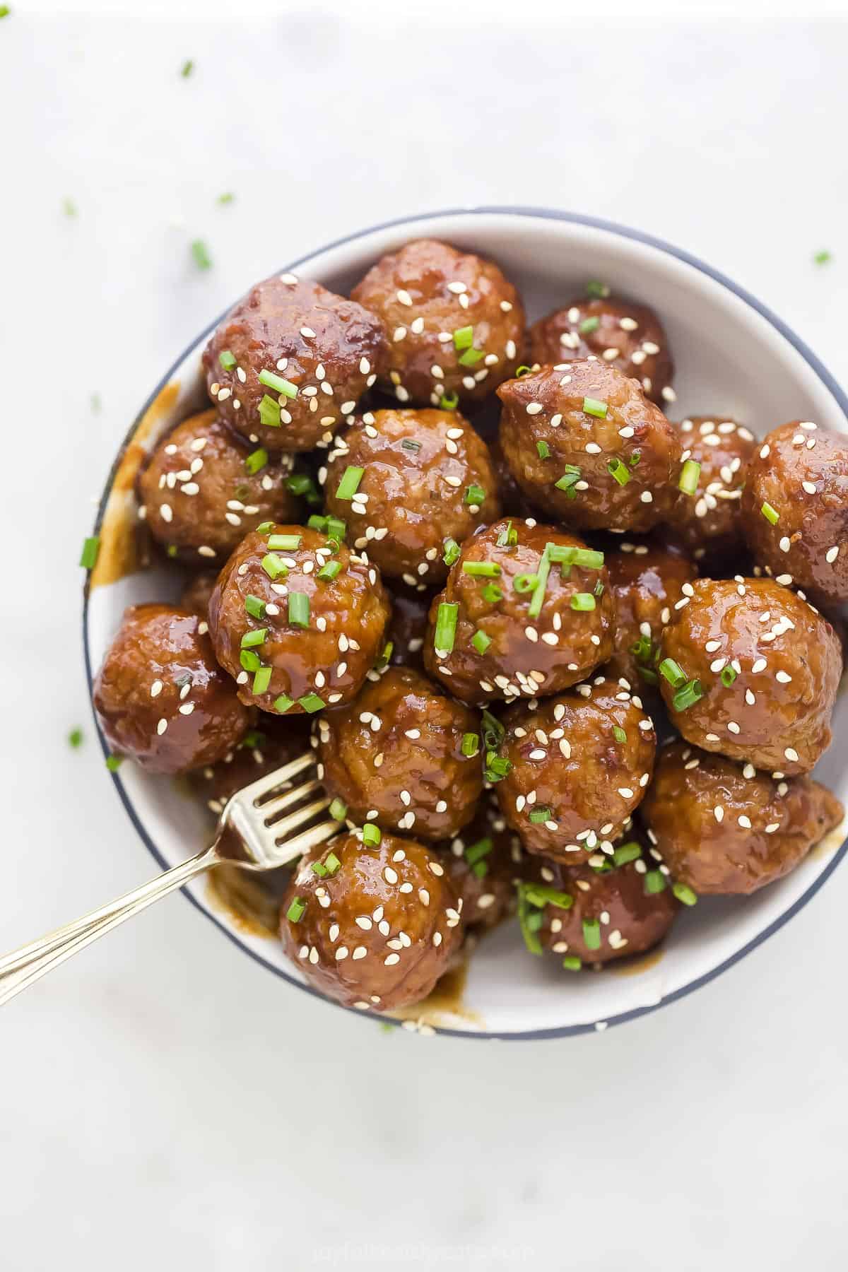 A bowl full of Crockpot Asian meatballs garnished with chopped chives and sesame seeds